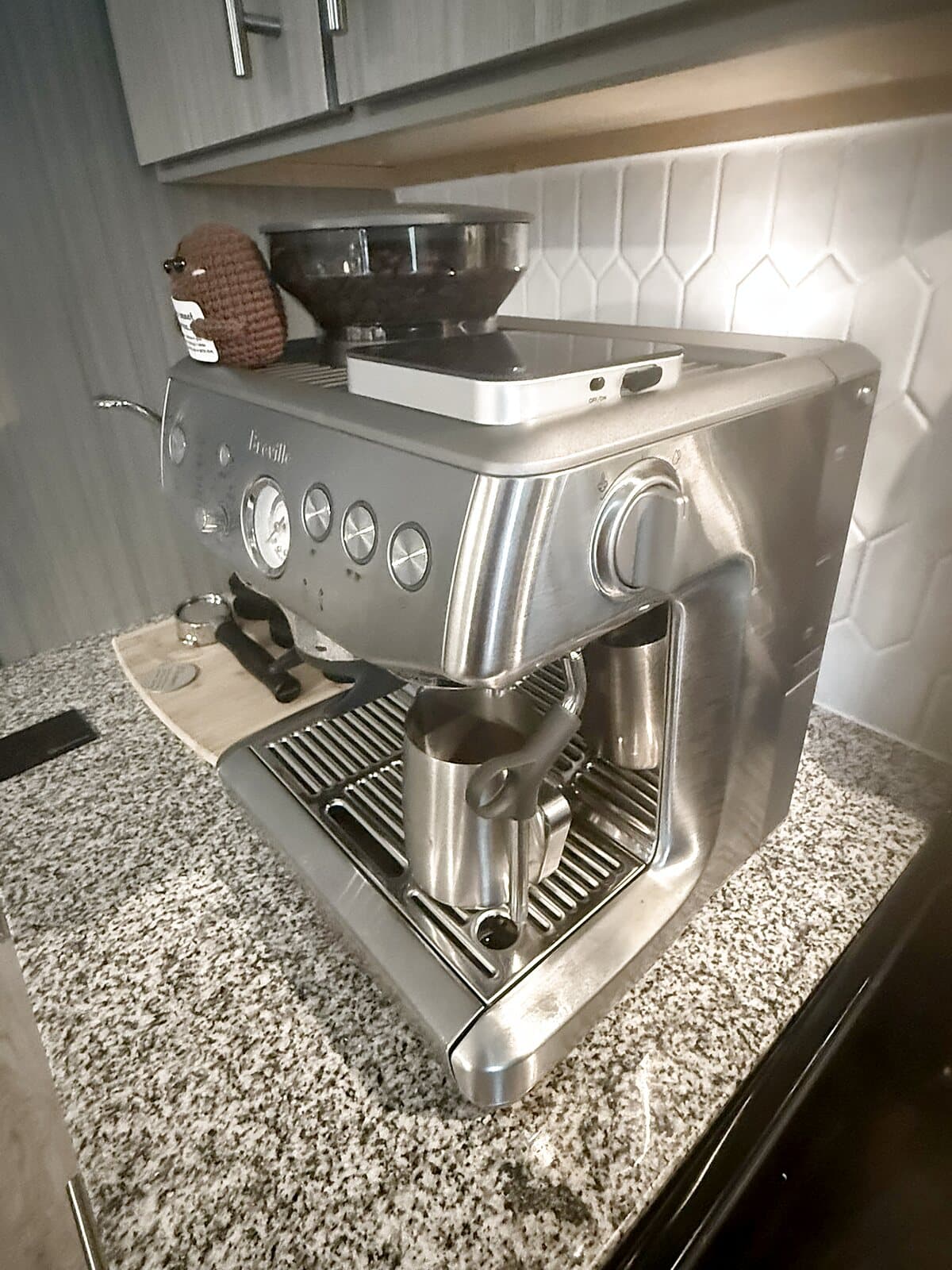 Breville Barista Express Impress on a granite counter with dark beans in the hopper and a scale on top