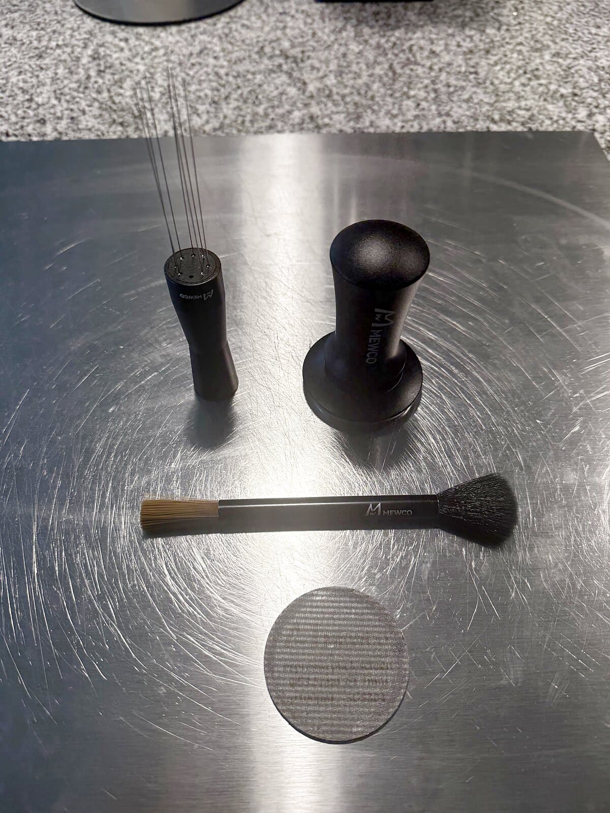 A 53.3mm distribution tool, tamper and puck screen on a steel board, all sized for Breville baskets